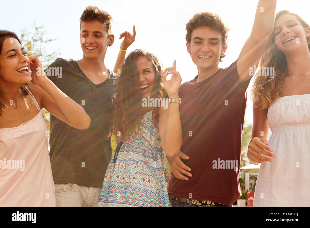 Group Of Teenage Friends Dancing Outdoors Against Sun Stock Photo
