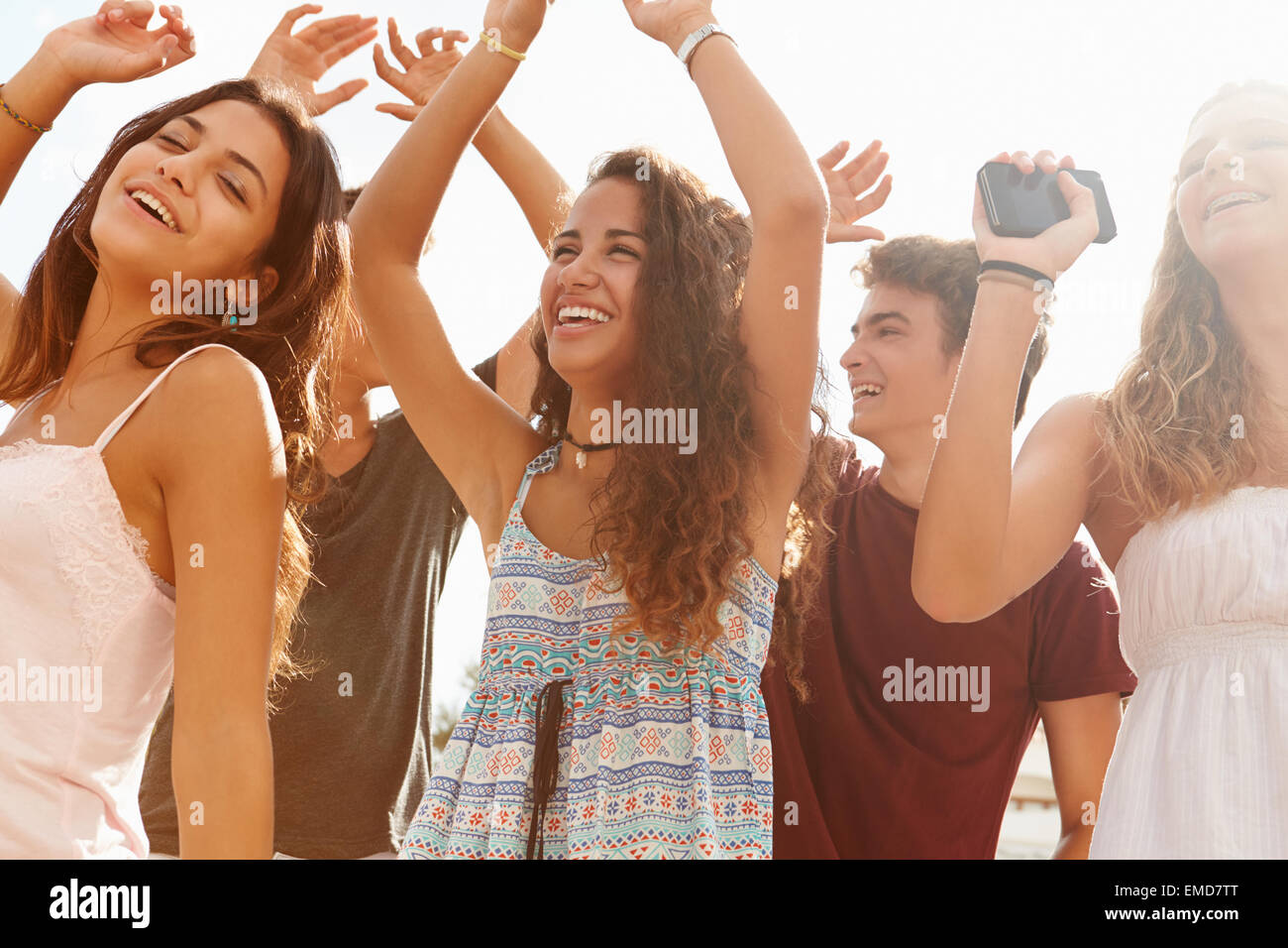 Group Of Teenage Friends Dancing Outdoors Against Sun Stock Photo