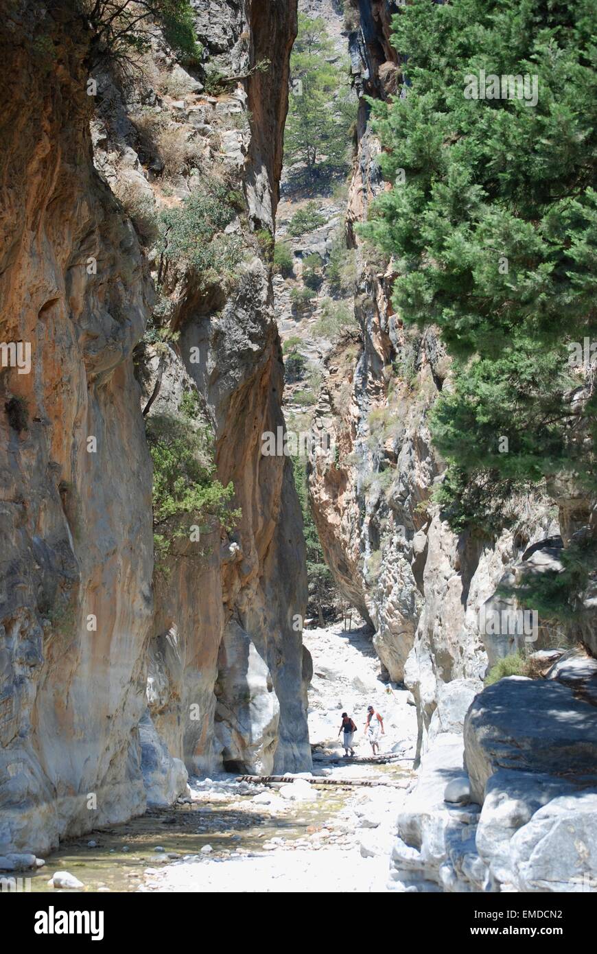 People walking along a hot dry riverbed at a narrow pass between steep sides of the Samaria Gorge, South West Crete, Greece. Stock Photo