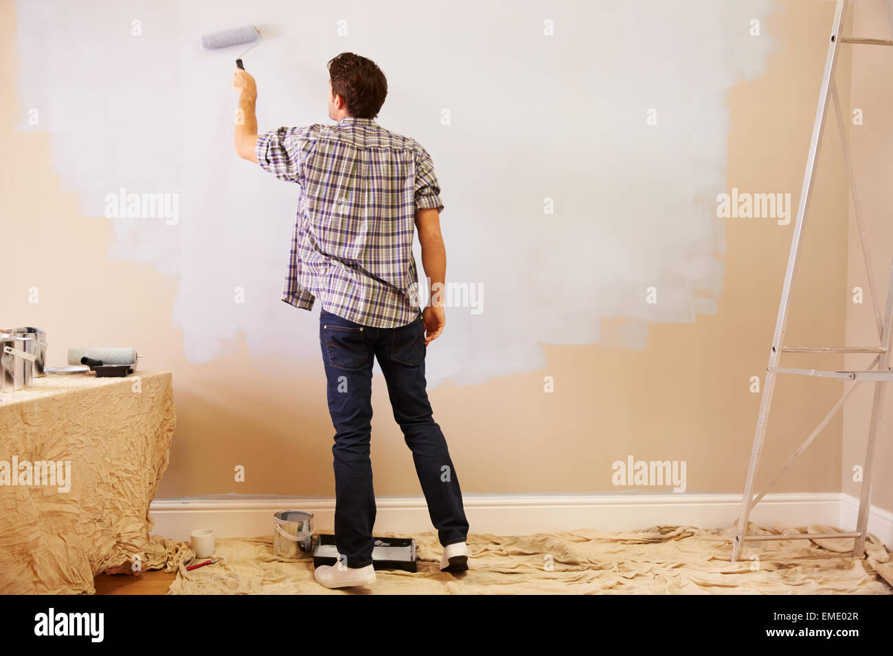 Man Decorating Room Using Paint Roller On Wall Stock Photo