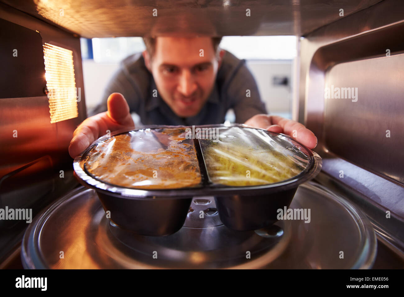 Man Putting TV Dinner Into Microwave Oven To Cook Stock Photo