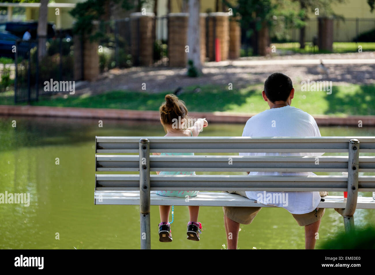 A Hispanic father and small daughter, sitting on a park bench, enjoy a spring day in a park. Oklahoma, USA. Stock Photo