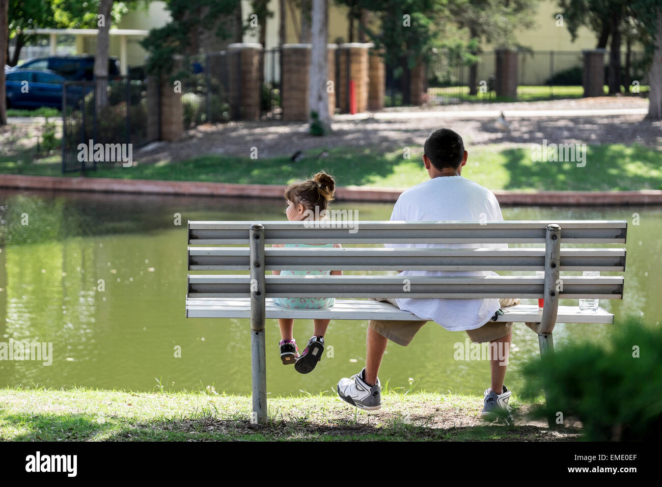 A Hispanic father and small daughter, sitting on a park bench, enjoy a spring day in a park. Oklahoma, USA. Stock Photo