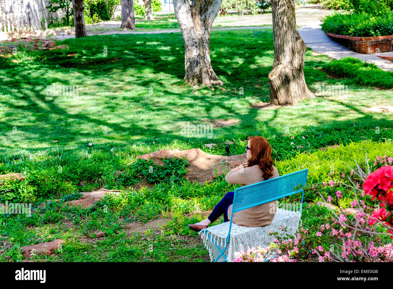 A Caucasian, red-haired woman sits on a bench and enjoys a Spring day in Will Rogers park in Oklahoma City, Oklahoma,USA. Stock Photo