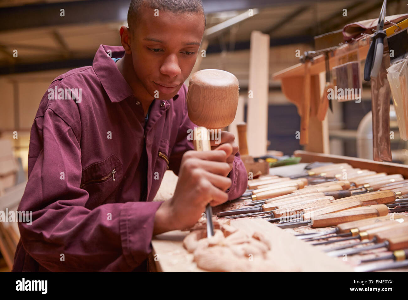 Apprentice Using Chisel To Carve Wood In Workshop Stock Photo