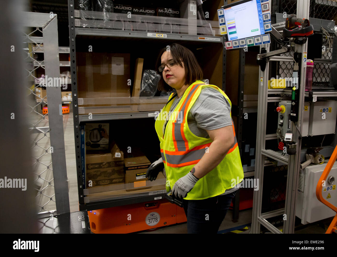 Female Hispanic employee at Amazon fulfillment center tracks packages in warehouse Stock Photo