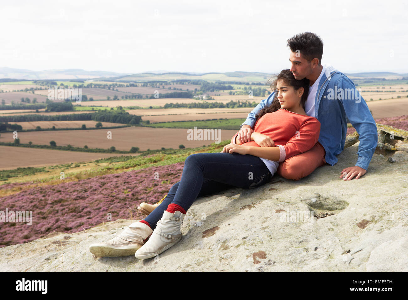 Young Couple Sitting On Rock Admiring View Stock Photo