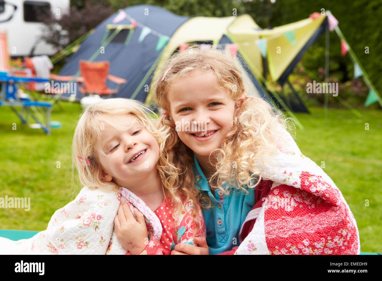 Two Girls Relaxing On Blanket During Family Camping Holiday Stock Photo