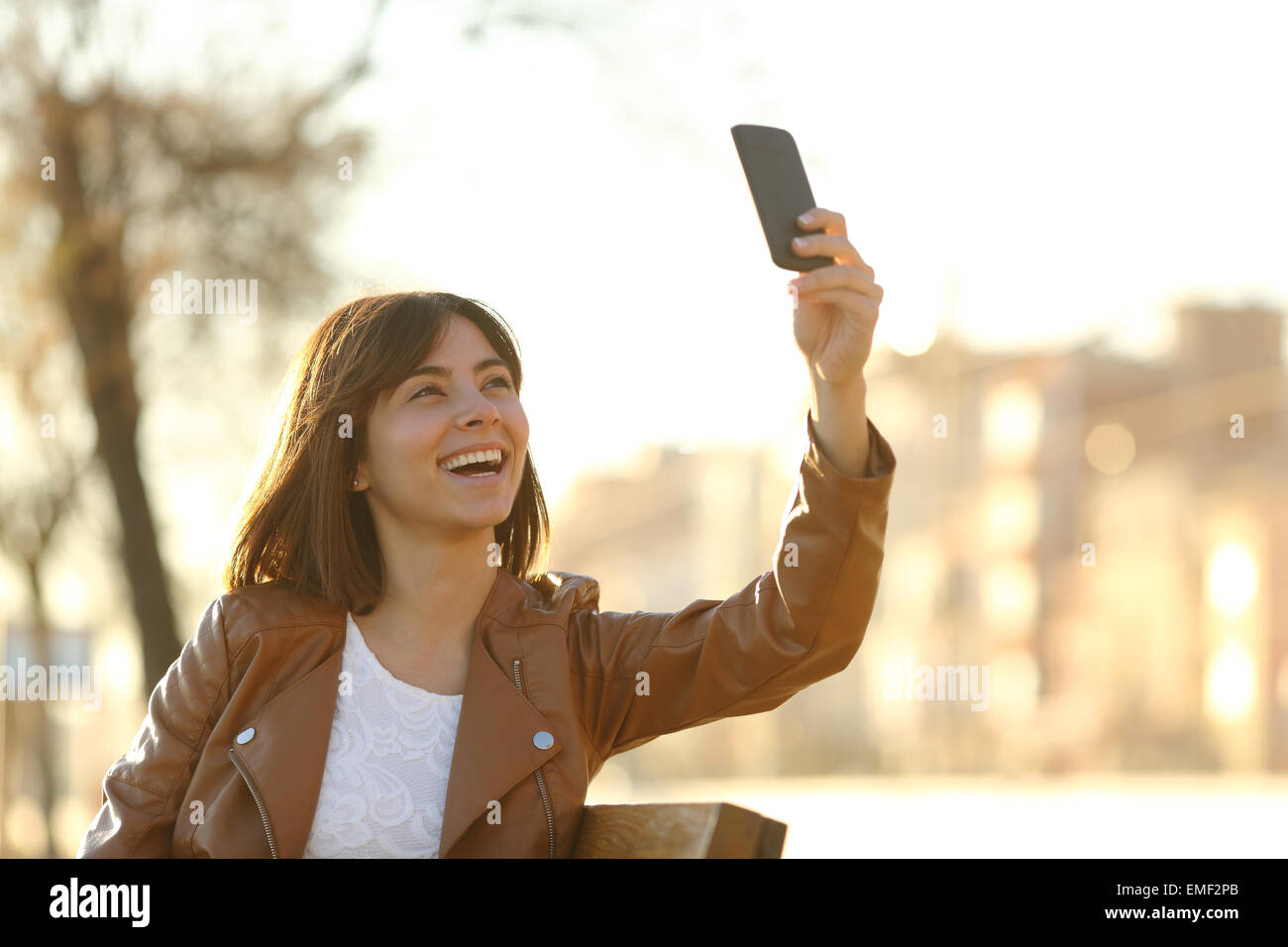 Woman taking selfie photo with a smarphone in winter sitting in a bench in a park Stock Photo