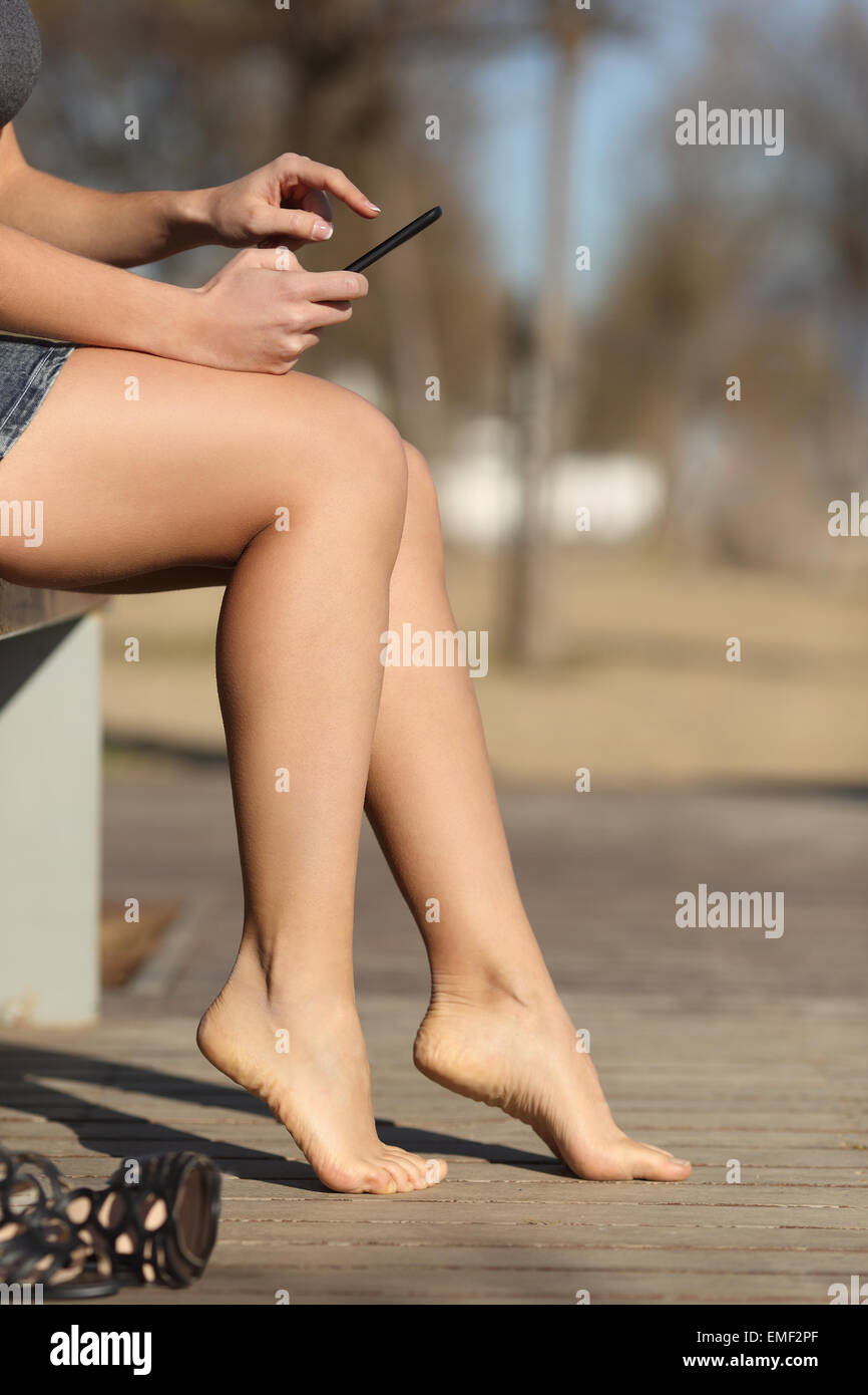 Woman using a smart phone relaxing in a park barefoot with an unfocused background Stock Photo
