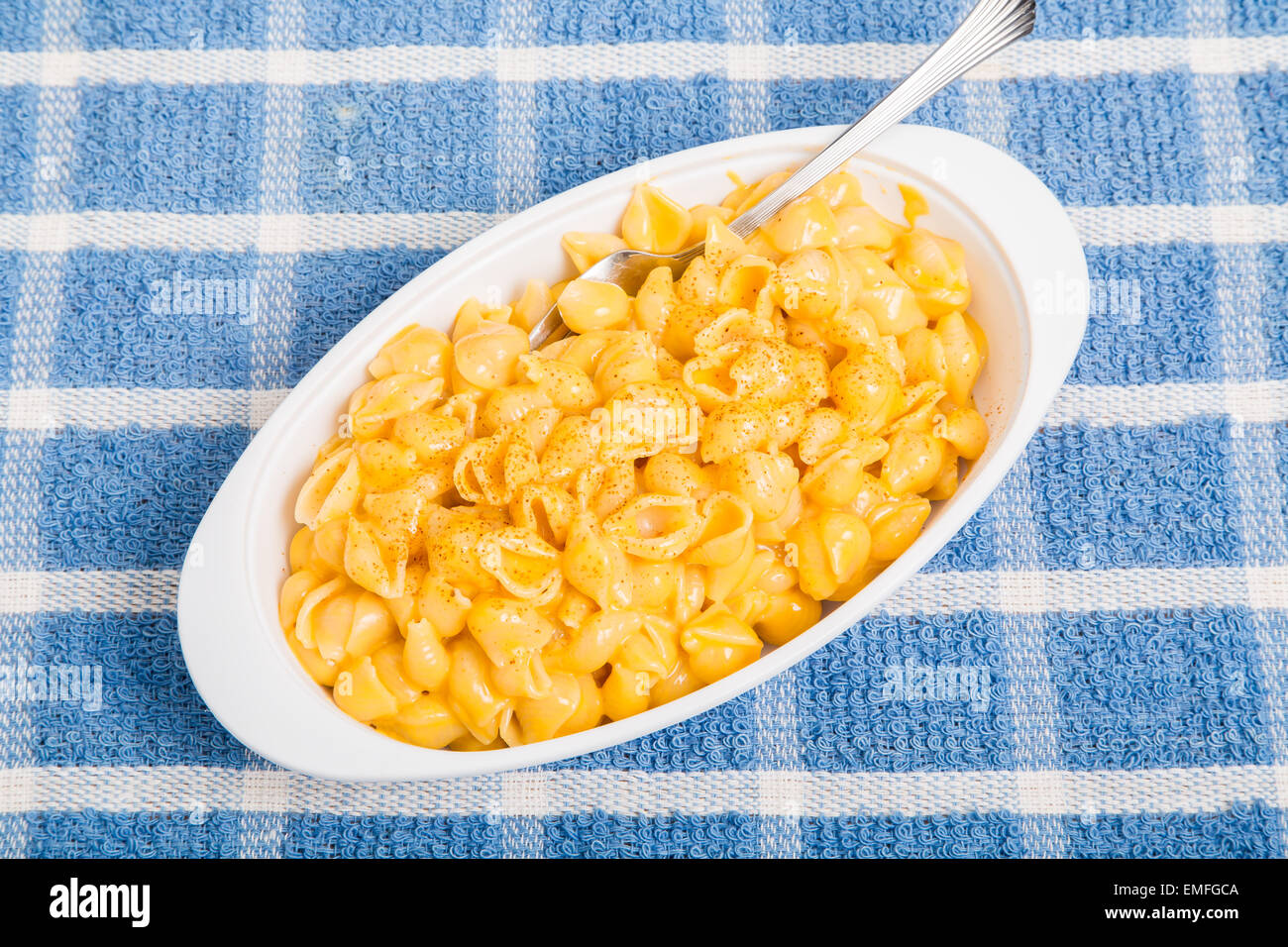 A white dish of macaroni and cheese with fork on blue plaid towel Stock Photo