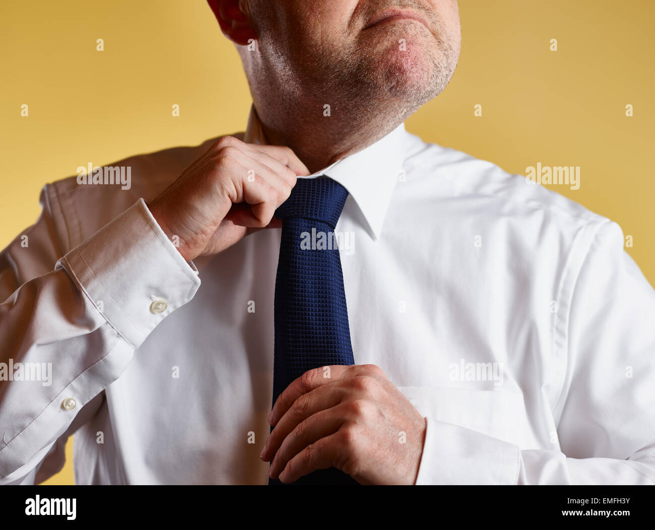 Close up, male wearing white shirt and blue tie, he loosen the tie knot, yellow background Stock Photo