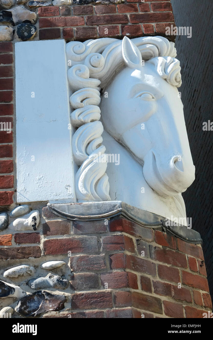carved stone horses head on corner of brick house wall Stock Photo