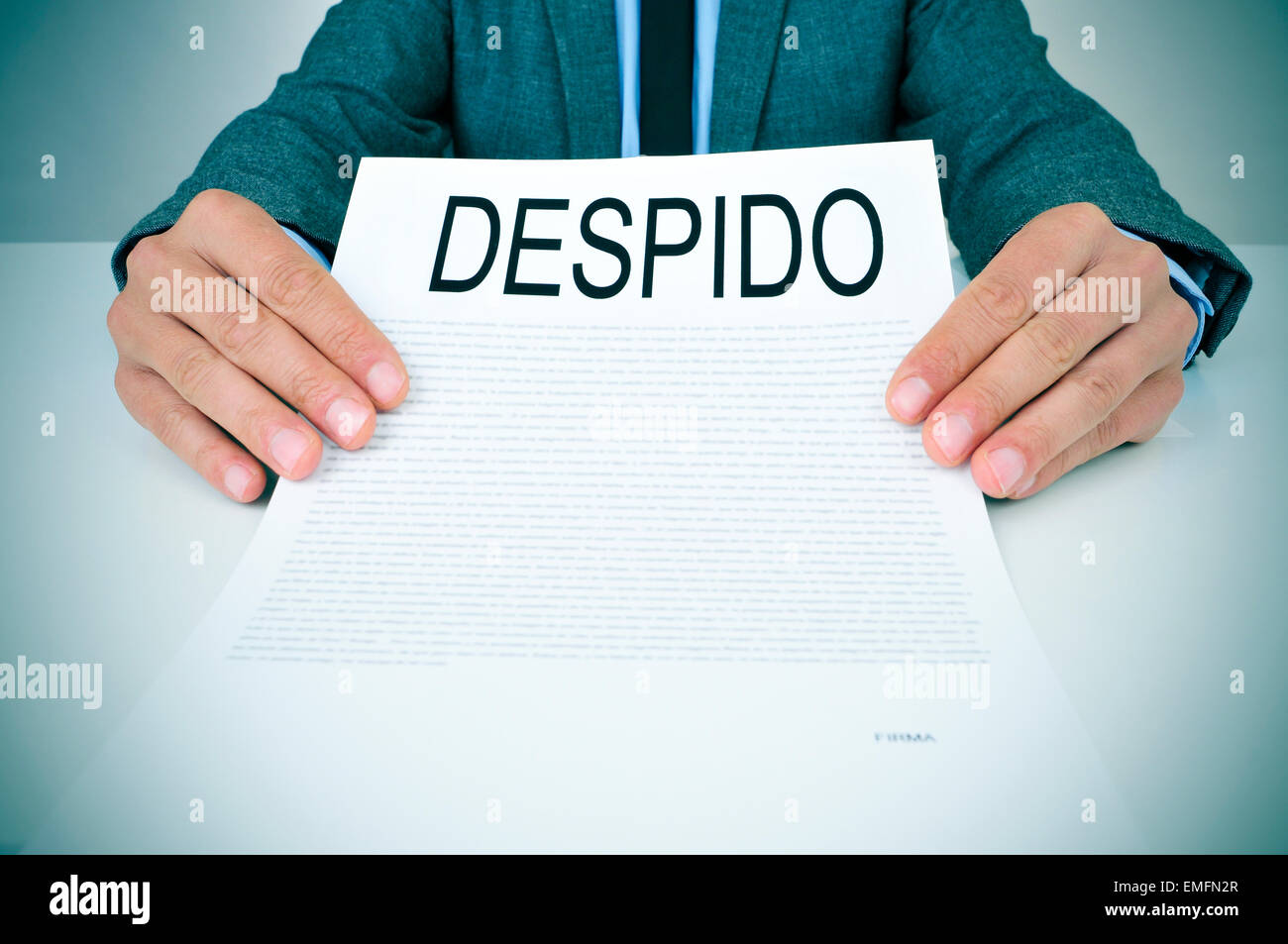 a young caucasian businessman in grey suit sitting at his office desk shows a document with the text despido, dismissal in spani Stock Photo