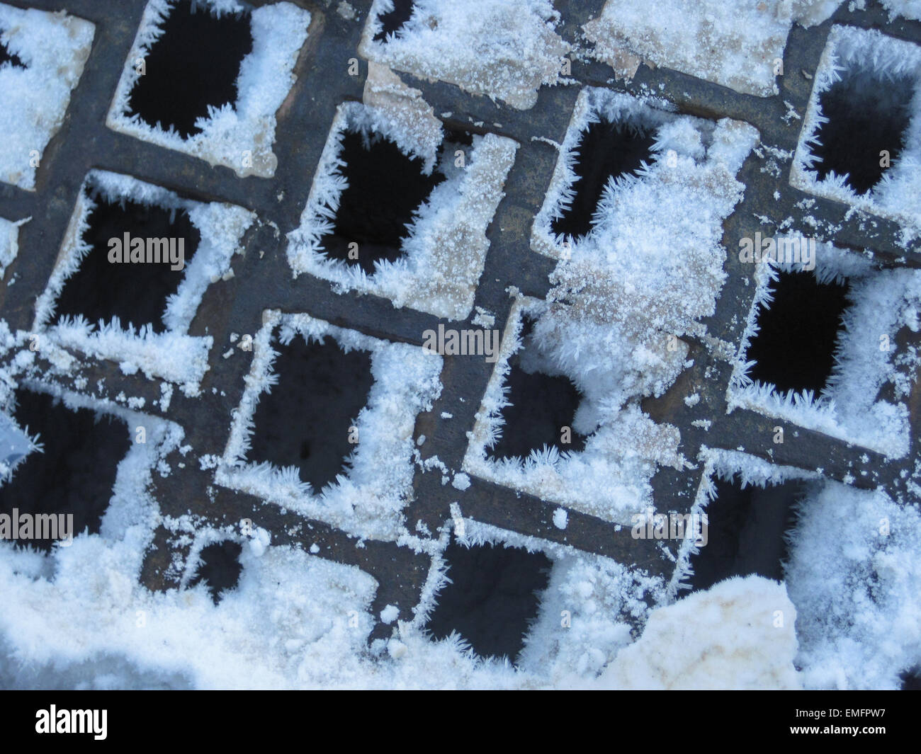 Snow and ice clump in the square holes of a metal grate Stock Photo