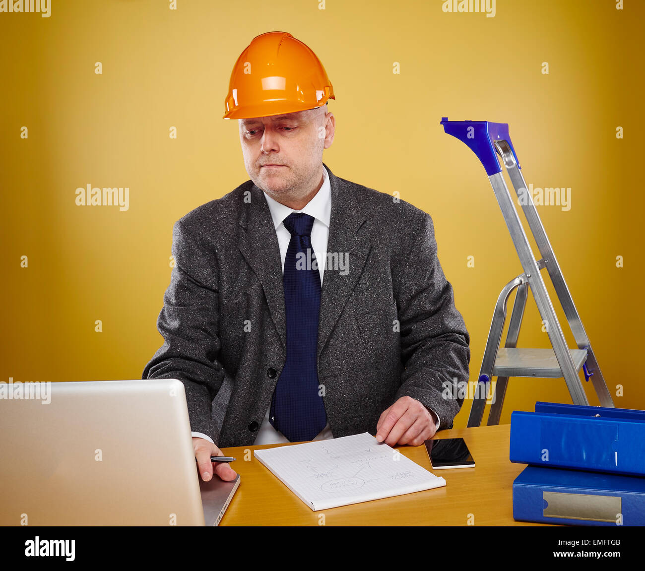 Working male engineer in office, he wearing a white shirt and tie and coat, head he wears a orange hard hat Stock Photo