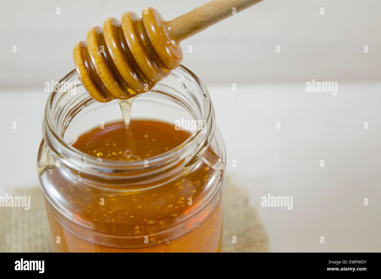 Honey dripping into a glass jar from a special wooden spoon Stock Photo