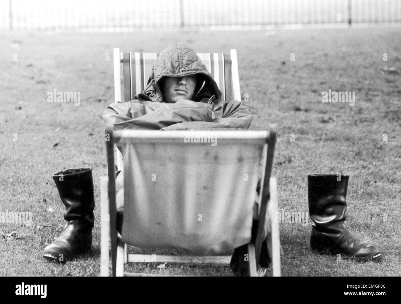 A weary traveller removes his boots as he takes a rest on a bed made from two deckchairs in St James Park. 5th August 1971. Stock Photo