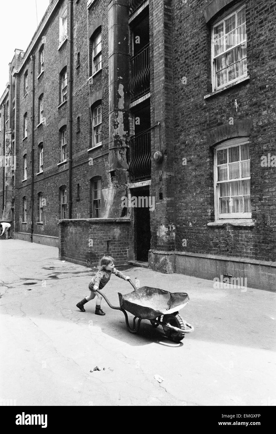 Two and a half year old Darren Haydn plays with his wheelbarrow outside the Great Eastern Buildings in Stepney, East London. 11th May 1976. Stock Photo