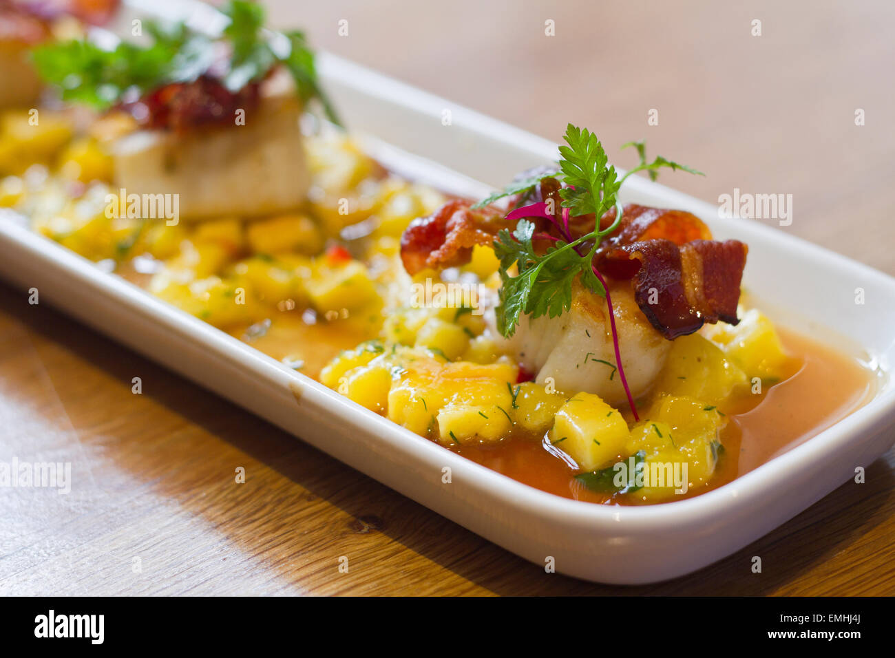 A plate of Scallops in a mango sauce topped with bacon Stock Photo