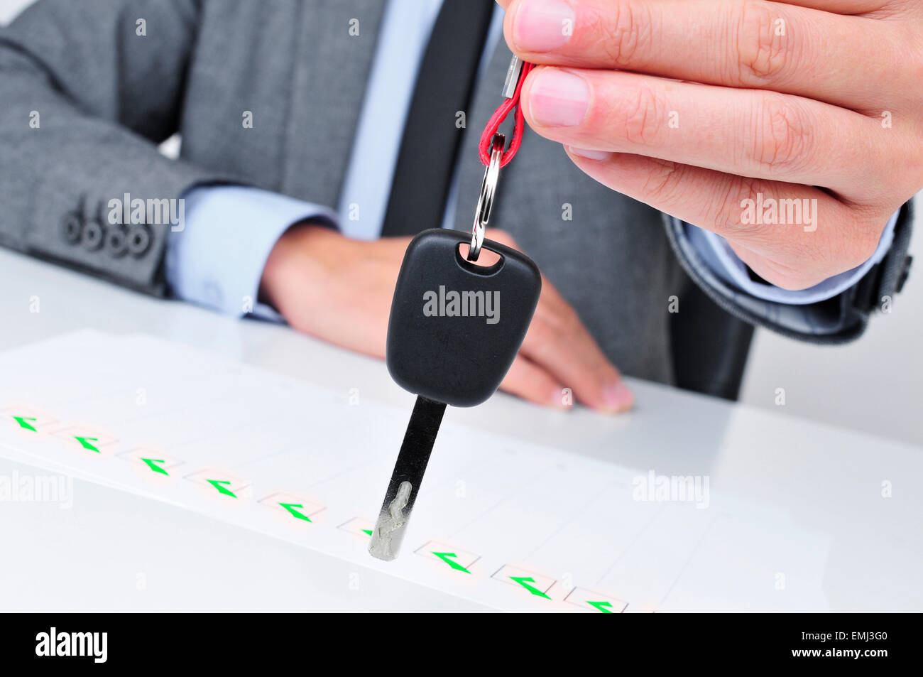 a young caucasian man in a grey suit sitting at his office desk gives a car key to the observer Stock Photo