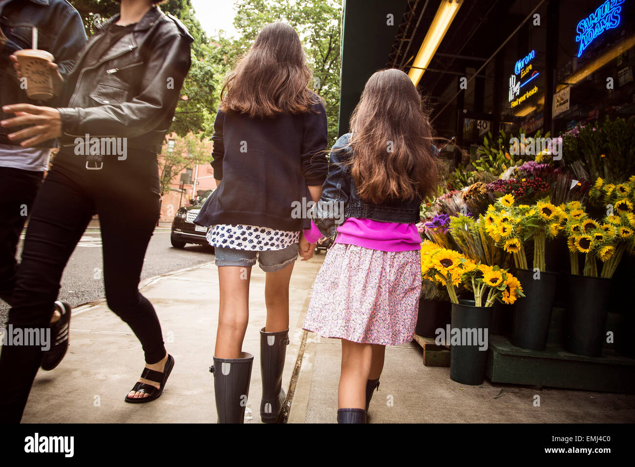 Two Young Girls Holding Hands While Walking Down Sidewalk Near Flower Stand, Rear View, New York City, USA Stock Photo