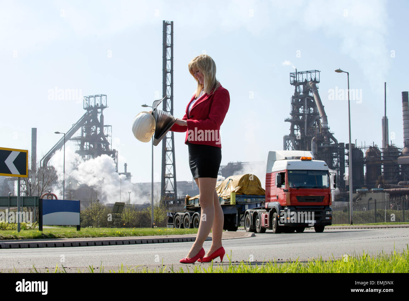 Businesswoman wearing a hard hat in an industrial environment with a backdrop of a steelworks Stock Photo