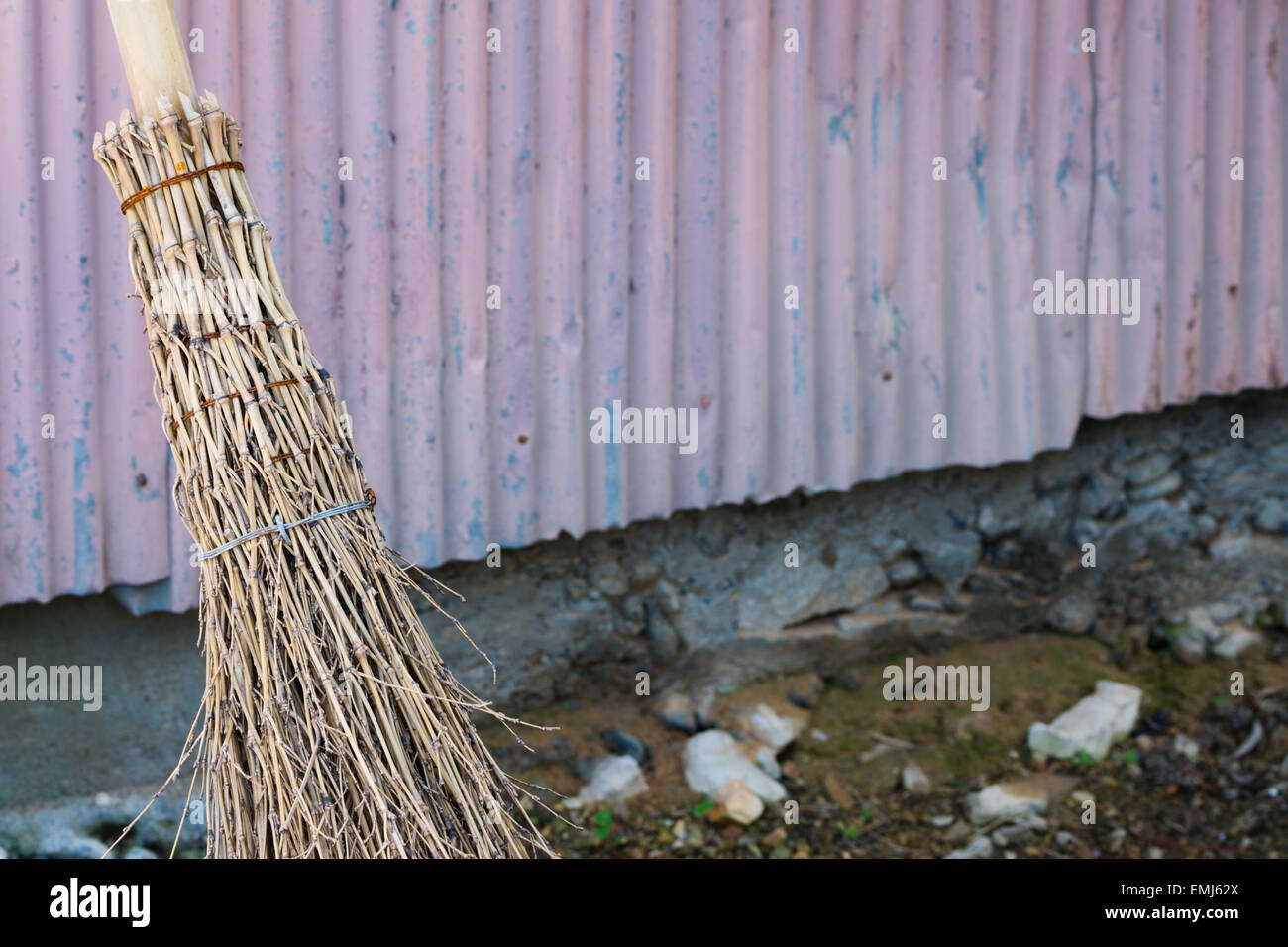 A straw bamboo broom leaning against an old wall outside. Stock Photo