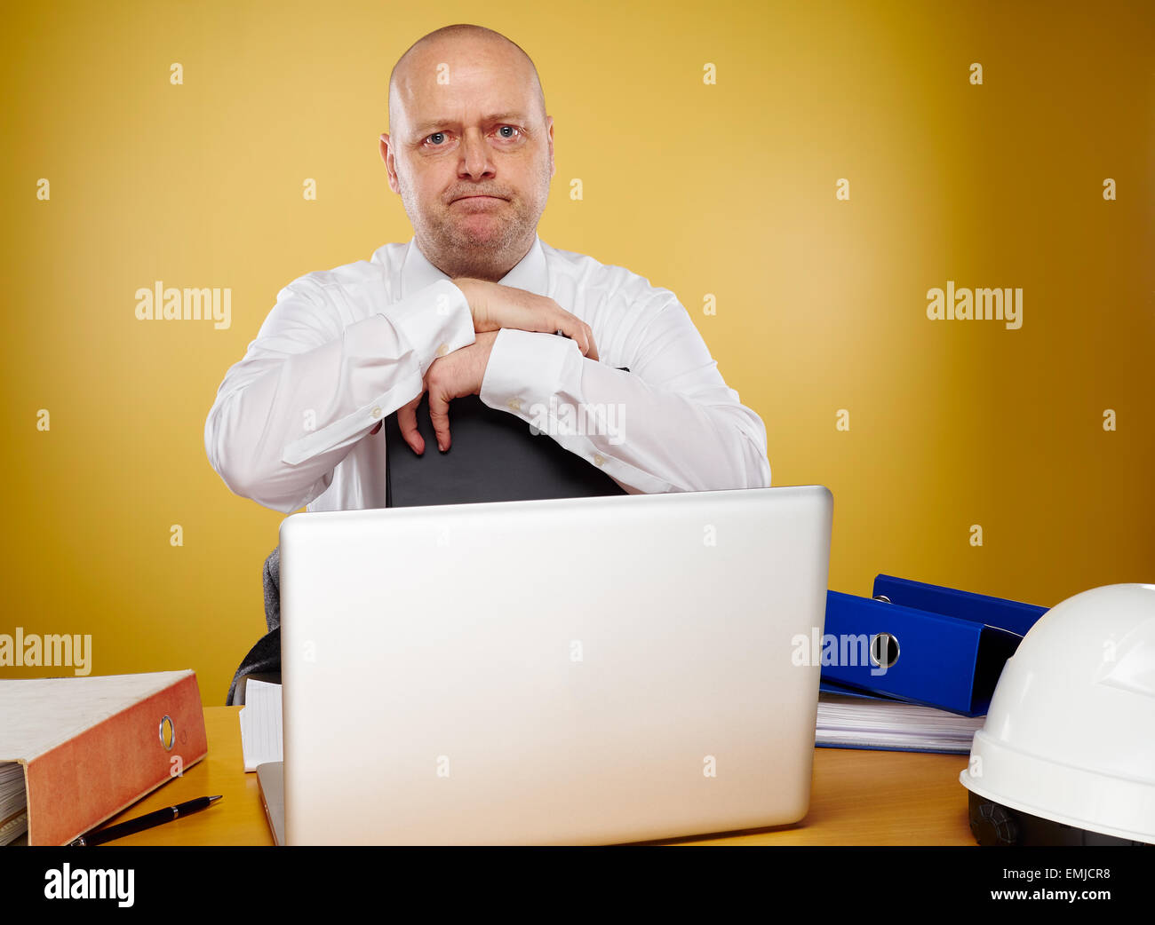 Hardworking male engineer in office, he wearing a white shirt and tie, the laptop, binders and white hard hat is on the table Stock Photo