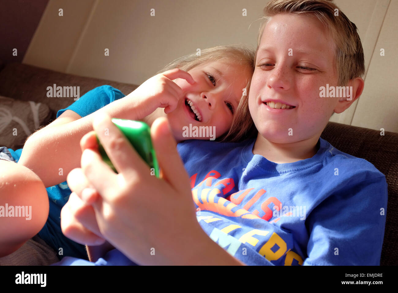 A boy and girl laugh and smile whilst playing on an iPod tablet Stock Photo