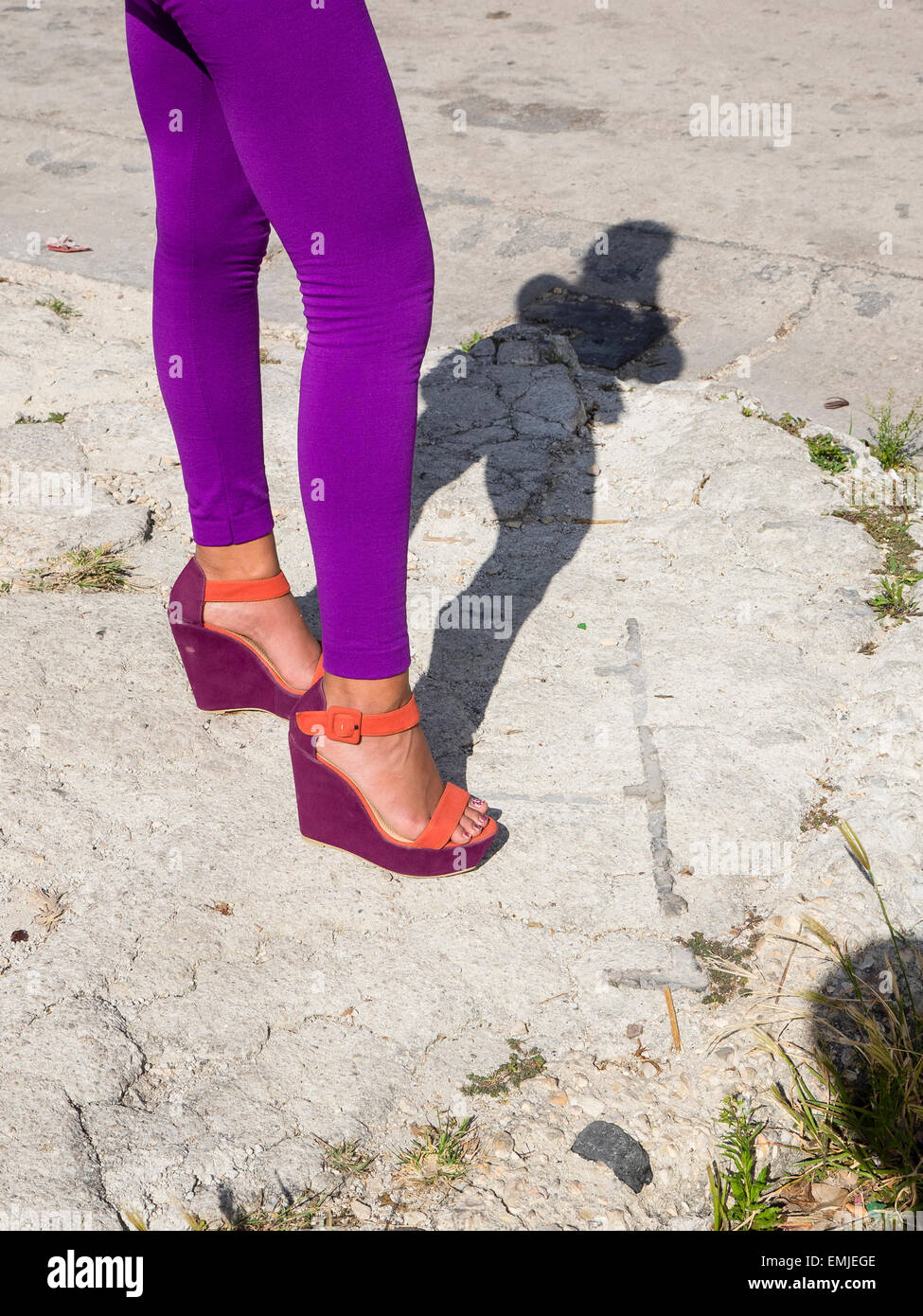 An image of a woman's purple tights, from waist down and purple and orange shoes. The woman casts a full figure shadow. Stock Photo