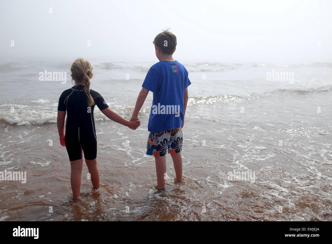 A young boy and girl holding hands look out to the sea on a misty day Stock Photo
