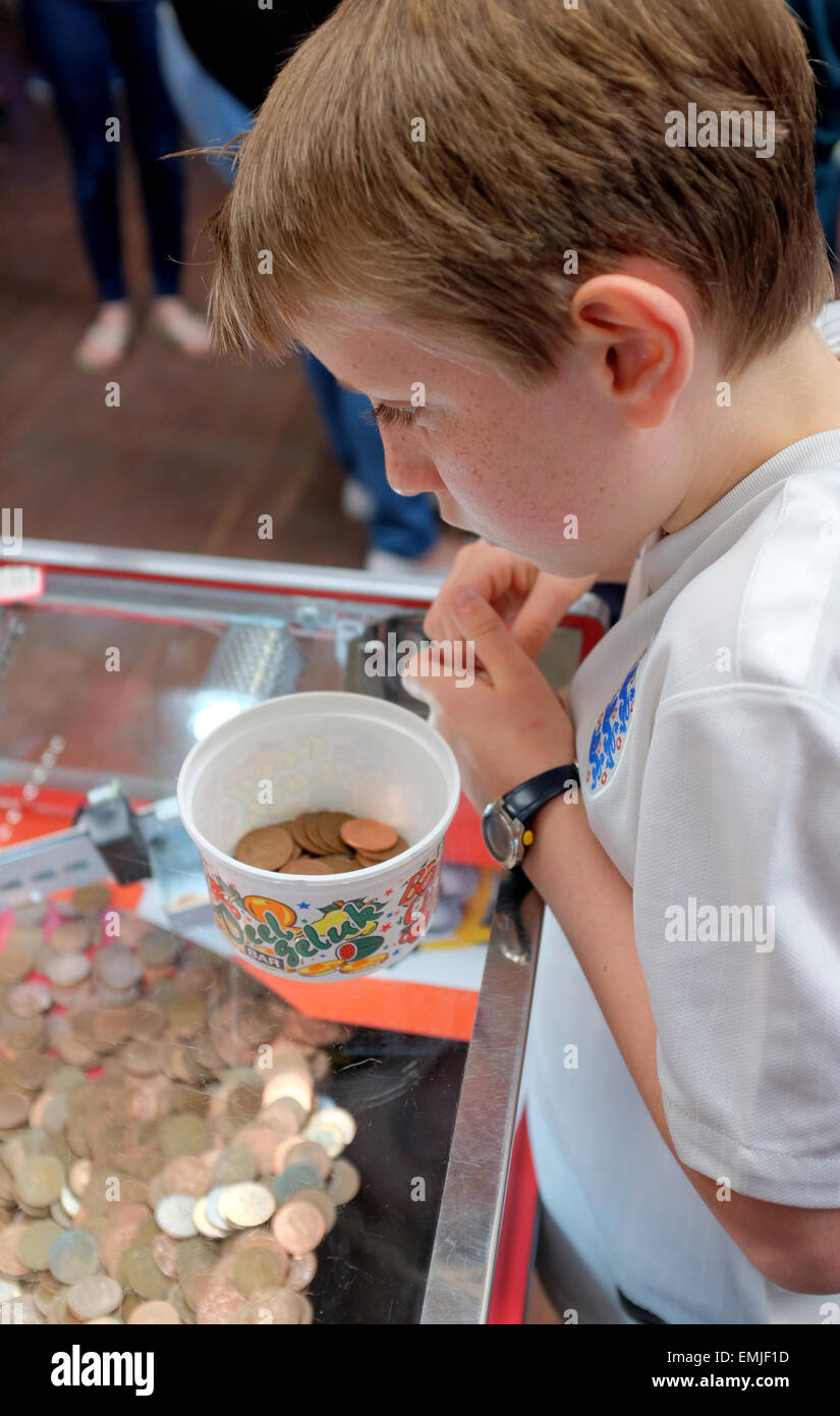 A boy playing putting Two pence coins in a tipping point machine in a seaside arcade Stock Photo