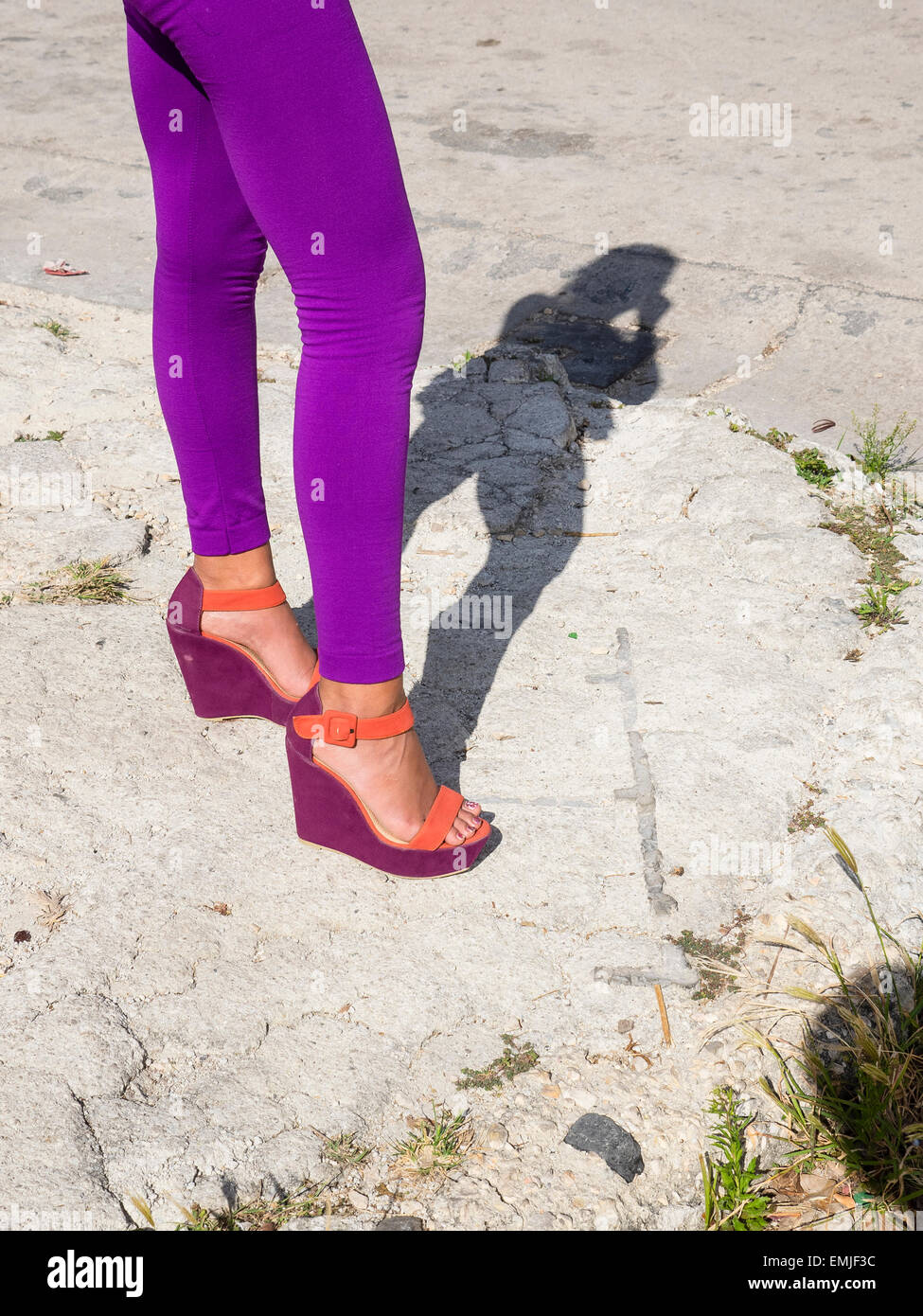 An image of a woman's purple tights, from waist down and purple and orange shoes. The woman casts a full figure shadow. Stock Photo
