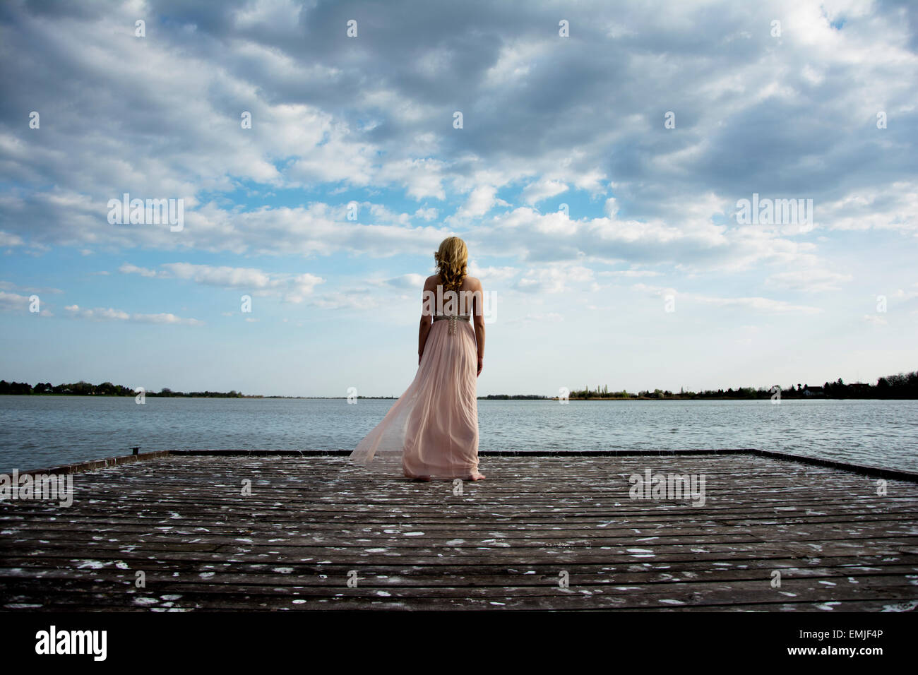 Back potrait of beautiful blond curly woman wearing evening peach color gown at lake.Fashionable and glamorous dress with chains Stock Photo