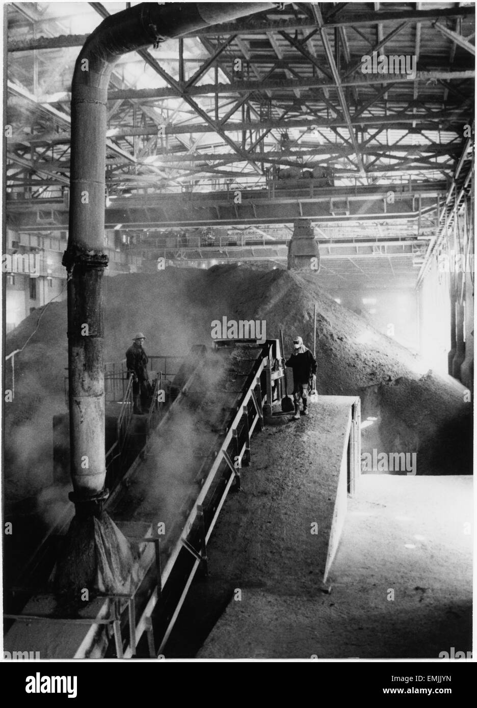 Dust Engulfing Workmen as Large Deposits of Phosphorous Fertilizer is Poured on to Conveyor Belts, Nanking Chemical Industrial Company, East China, 1965 Stock Photo
