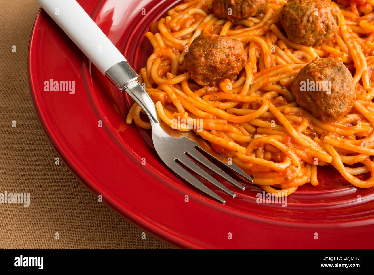A spaghetti and meatball TV dinner on a red plate with a fork on a tan