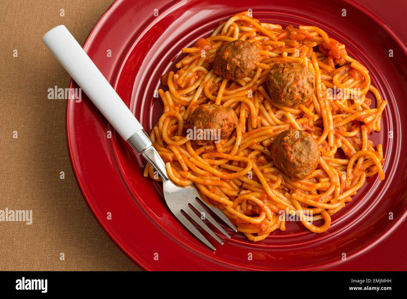 Top view of a spaghetti and meatball TV dinner on a red plate with a fork on a tan table cloth. Stock Photo