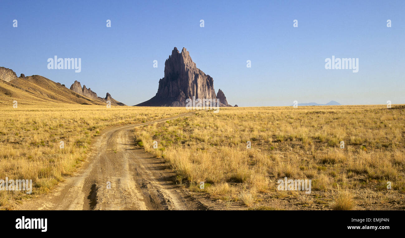 A rutty dirt road leads to Shiprock, a volcanic peak on the Navajo Indian Reservation in northern New Mexico. Also called the Rock With Wings by the Navajos, the peak is considered sacred. In the background is Sleeping Ute Mountain, considered sacred by the Ute Indians. Stock Photo