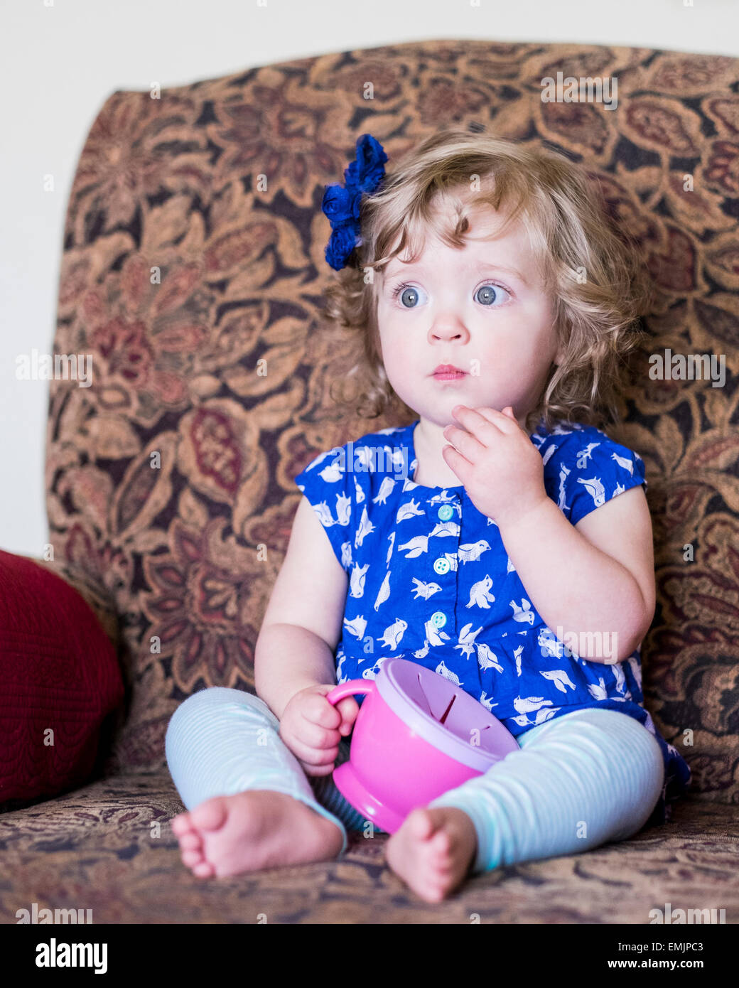A beautiful 14 month old Caucasian girl sits in a chair and eats