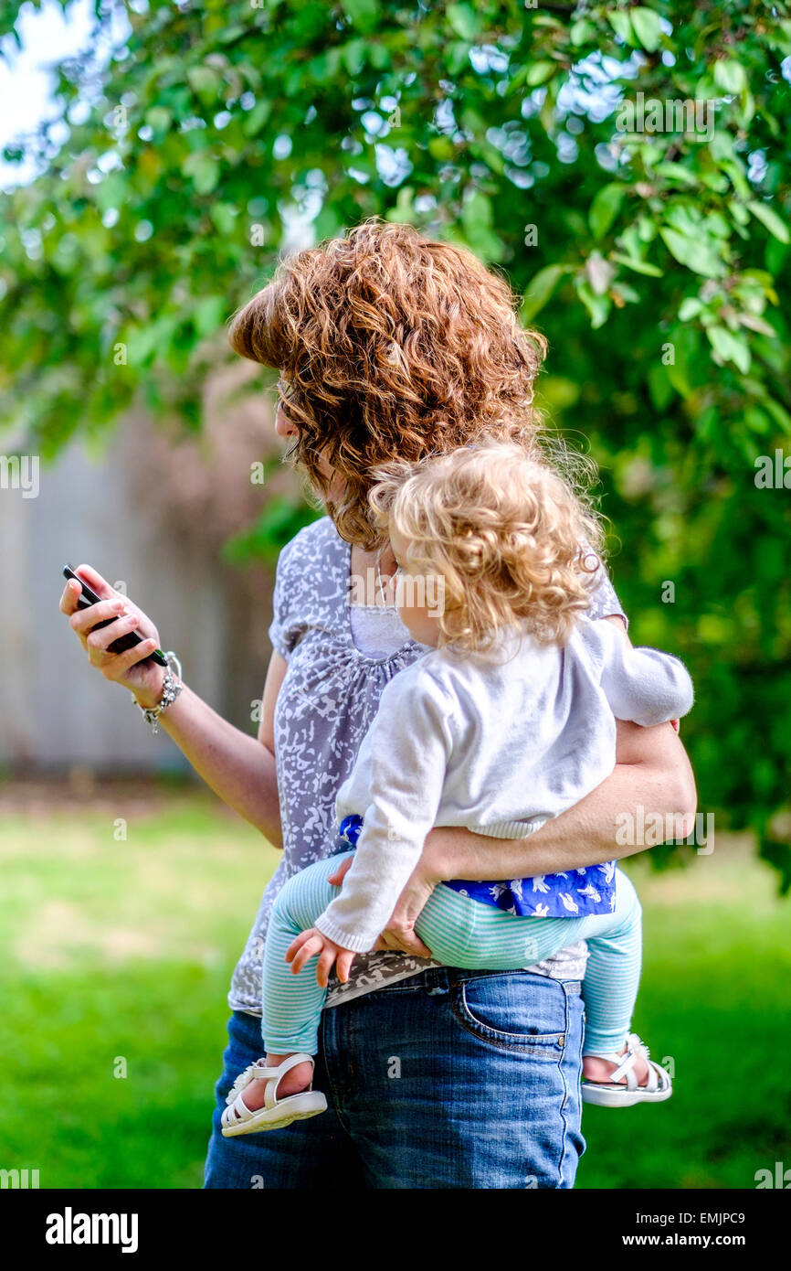 A 50 year old Caucasian grandmother holds her 14 month old granddaughter while making a mobile phone call outdoors. USA Stock Photo