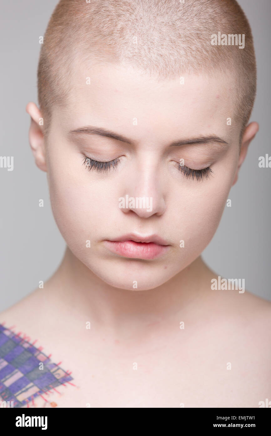 A young woman with a shaved head and tattoos on her shoulder, arms and ...