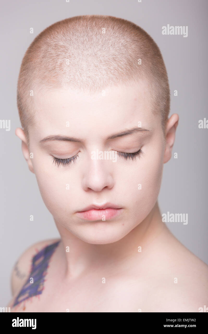 A young woman with a shaved head and tattoos on her shoulder, arms and ...