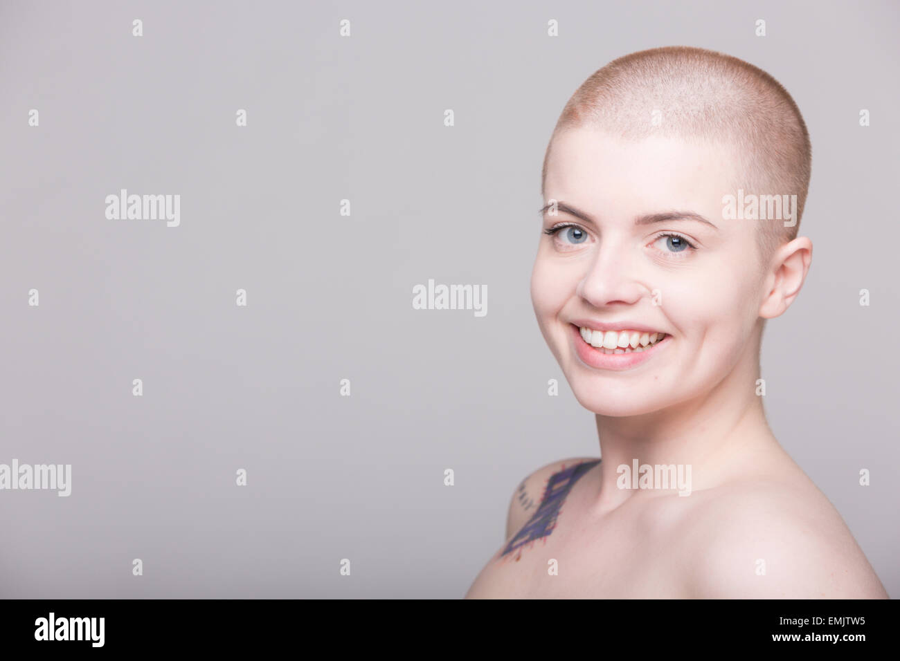 A young woman with a shaved head and tattoos on her shoulder, arms and ...