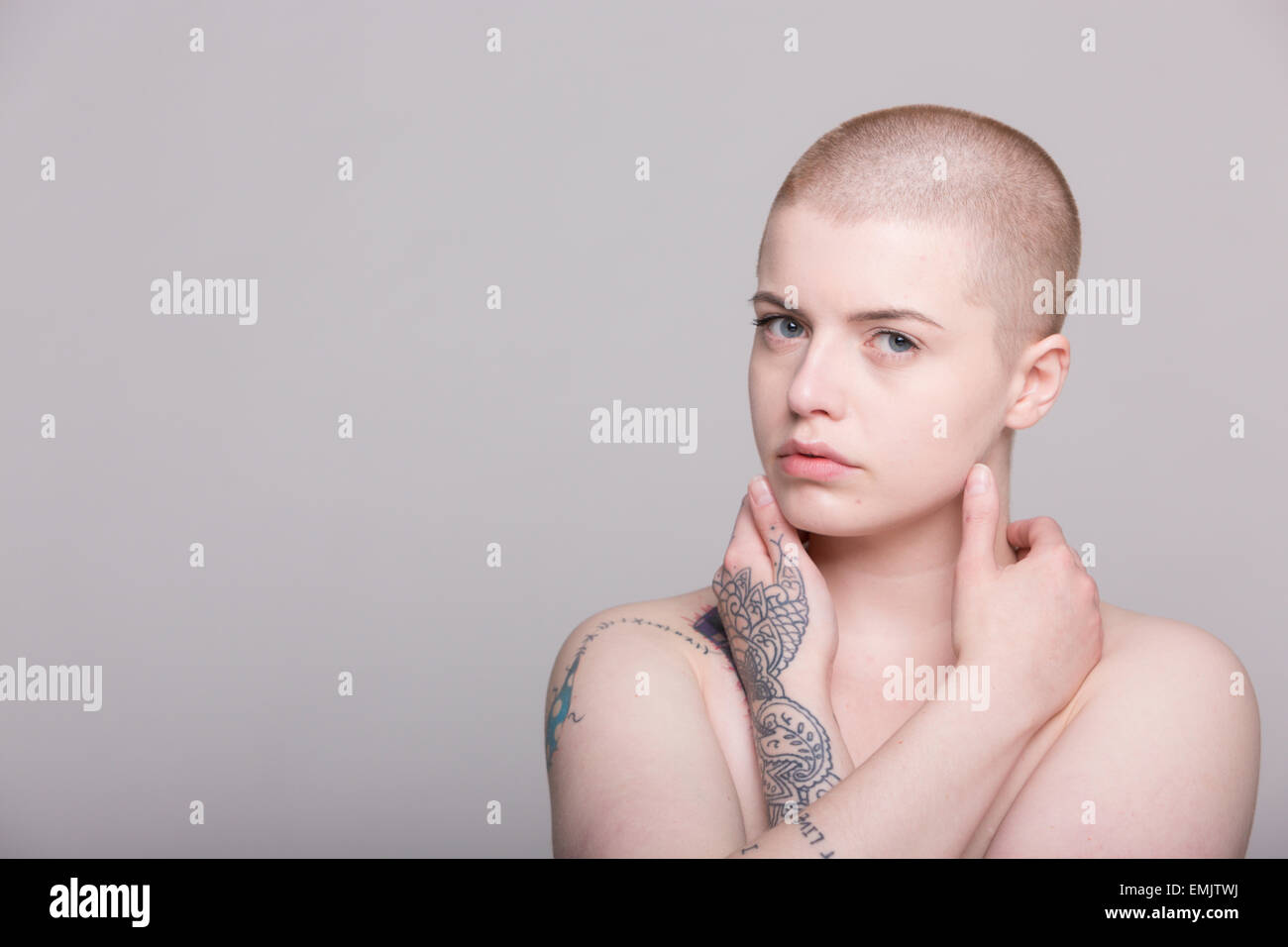 A young woman with a shaved head and tattoos on her shoulder, arms and ...