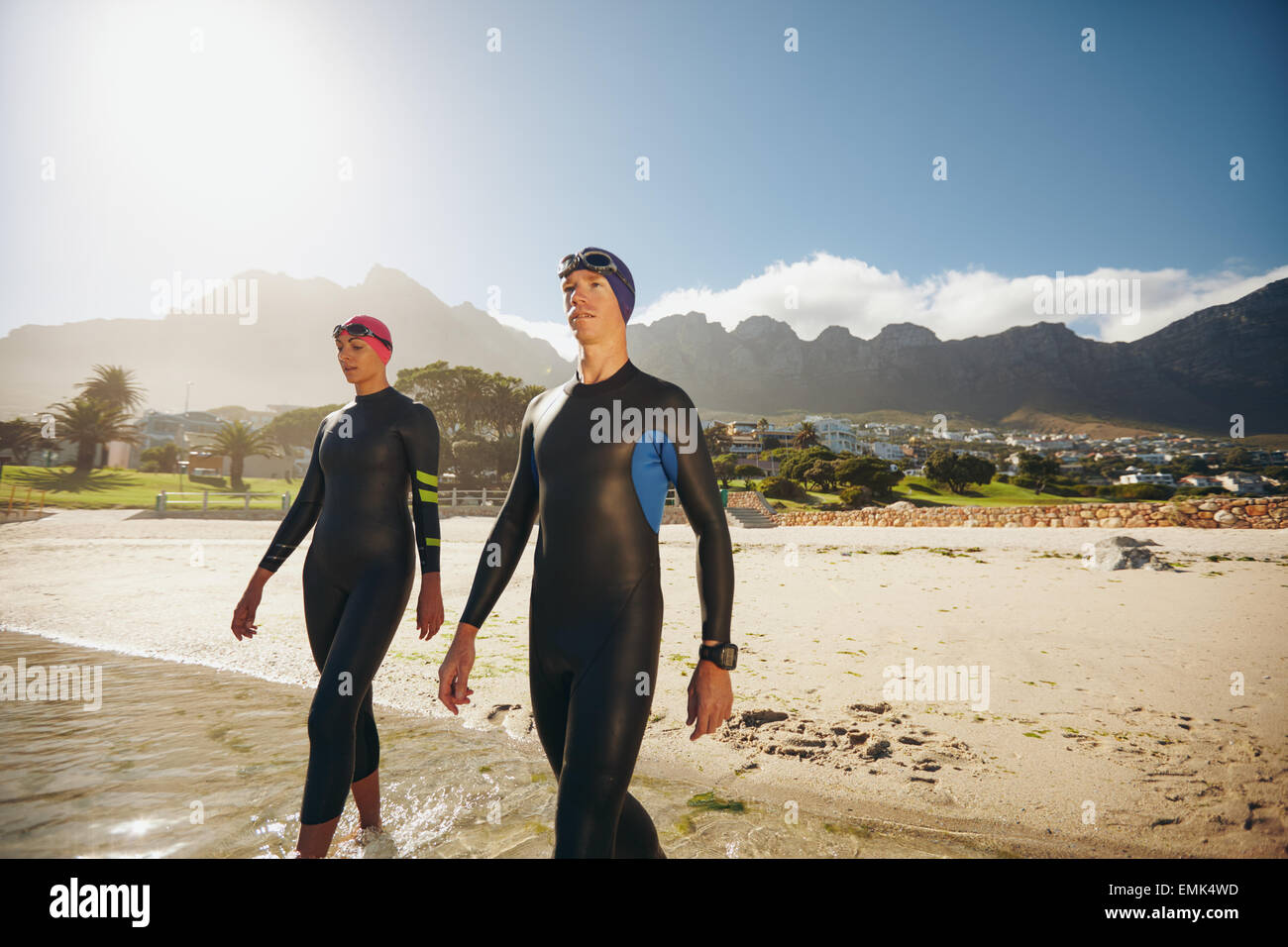 Image of two young triathletes walking into the sea wearing wetsuit. Man and woman doing triathlon training at the beach. Stock Photo