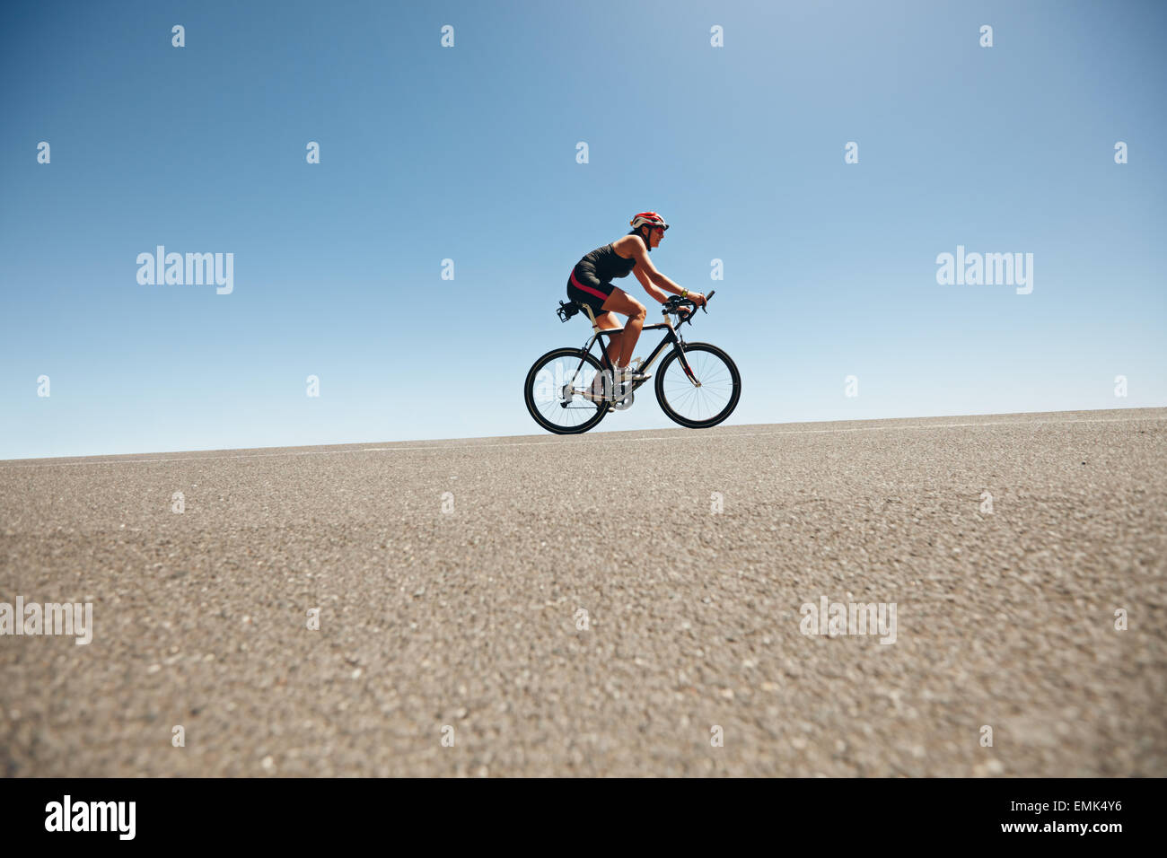 Female cyclist on a country road training for triathlon. Young woman riding bicycle up hill. Stock Photo