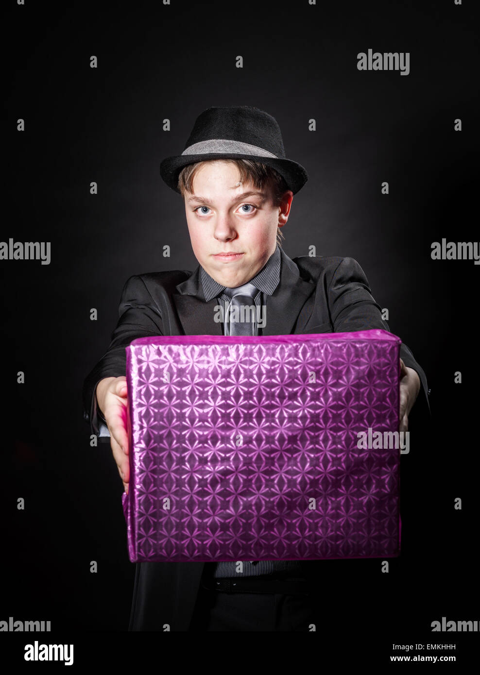 Expressive teenage boy holding box with gift isolated on black Stock