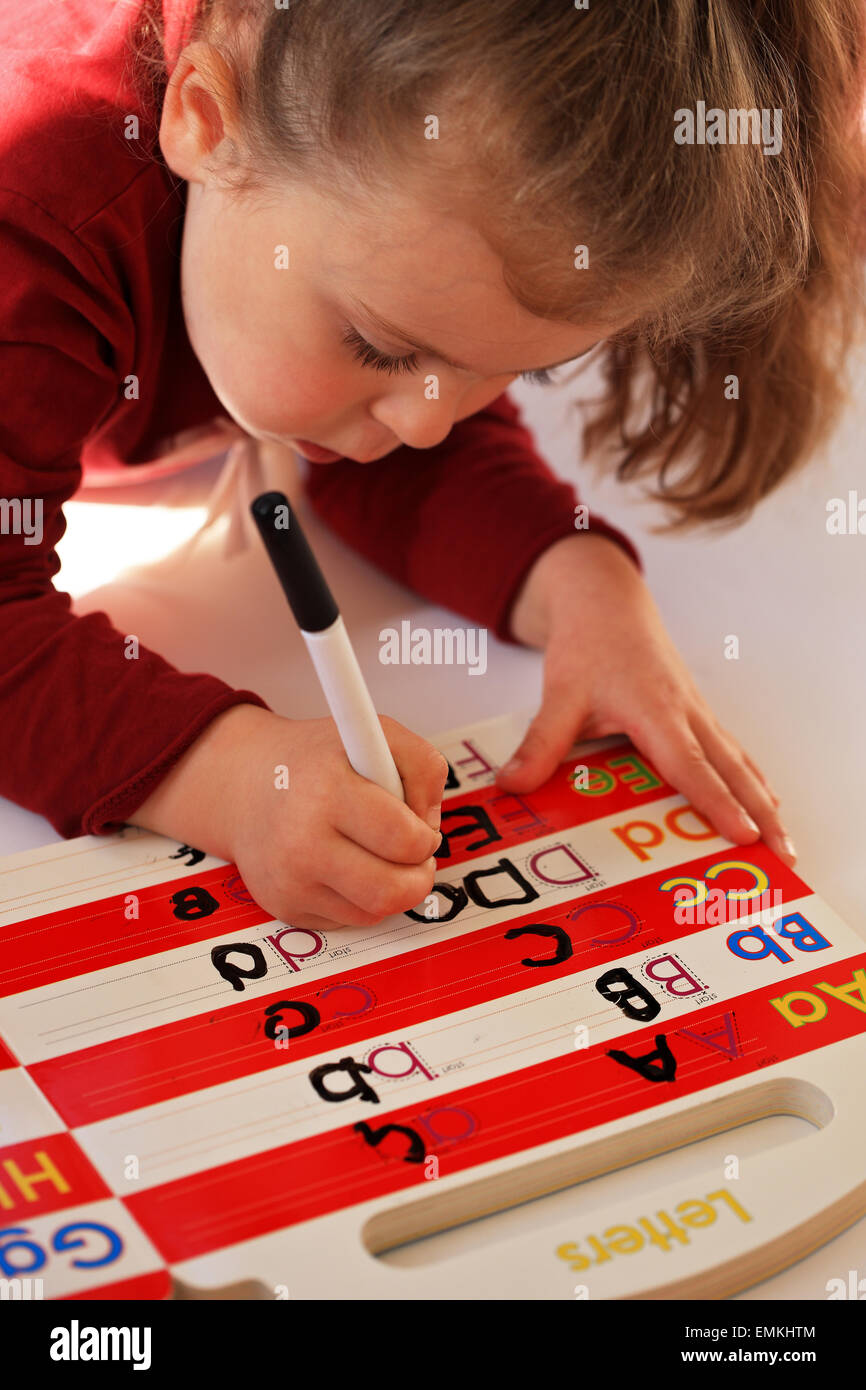 Four year old girl learning and practicing her letters on a wipe clean book Stock Photo