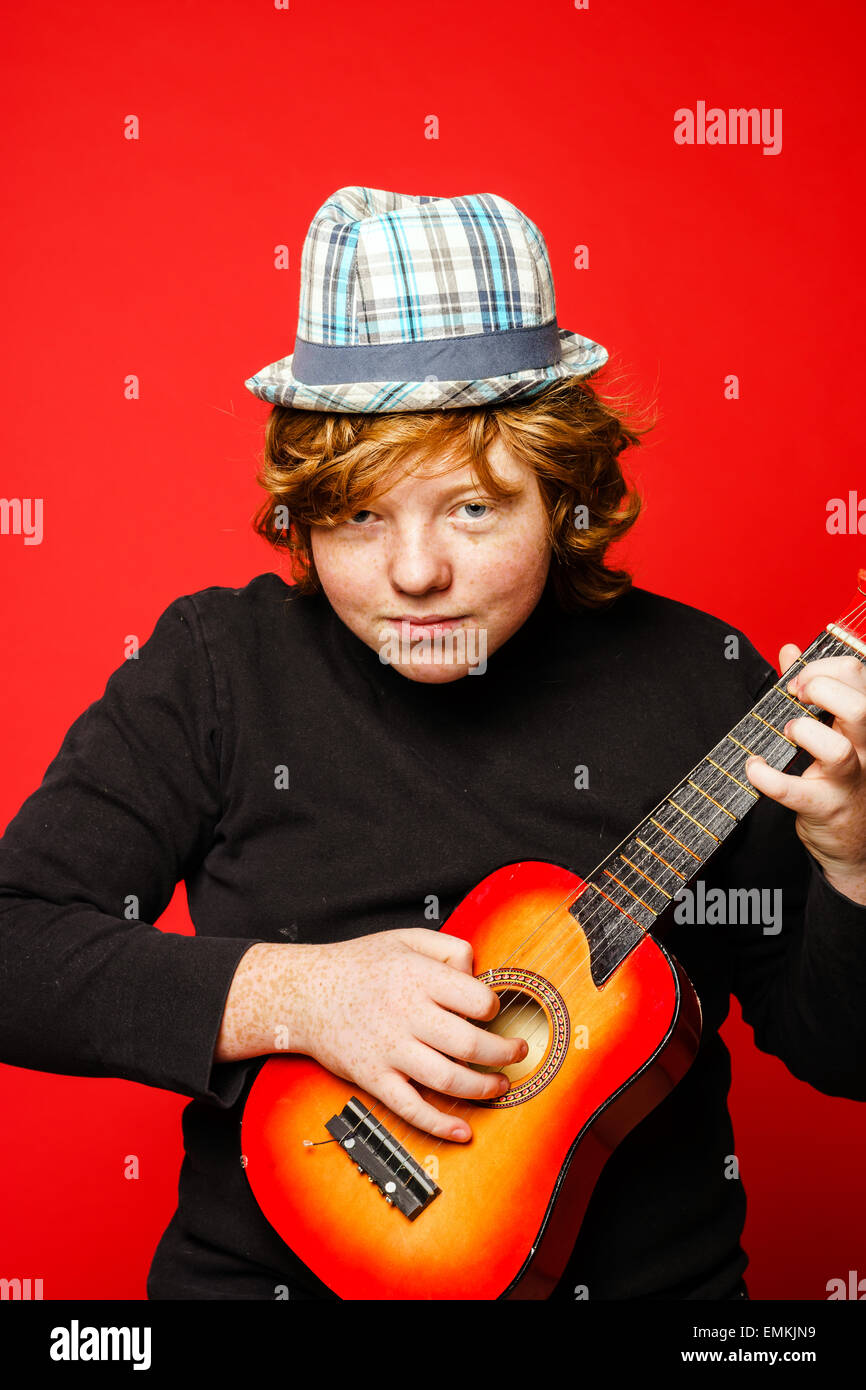 Red-hair funny teenage boy playing little guitar, isolated on vivid red  background Stock Photo - Alamy